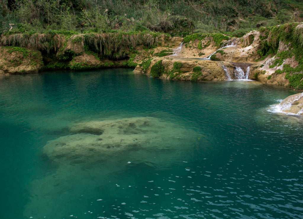 Turquoise water pool with limestone formations underwater surrounded by waterfalls in the rock covered with ferns, Mexico