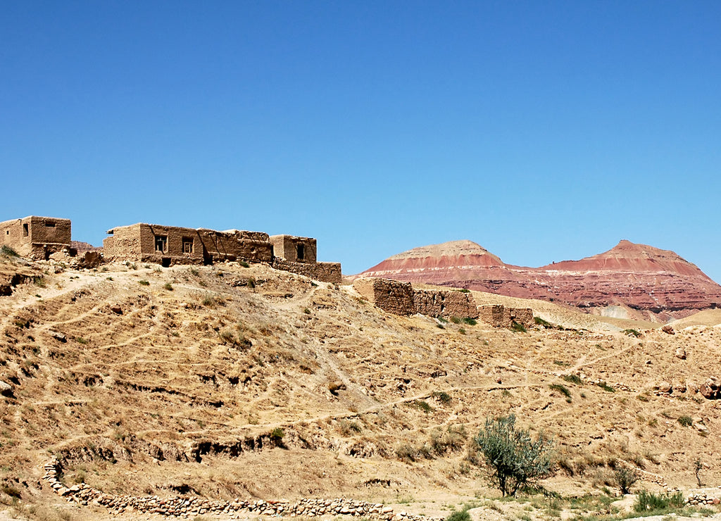 Village between Herat and Qala-e-Naw, Herat Province in Afghanistan with a backdrop of colorful red mountains in a very remote part of western Afghanistan. On the road from Herat to Bala Morgab