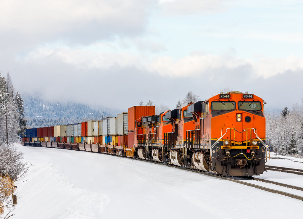 Winter scene of locomotive pulling freight cars close to Whitefish, Montana with fresh snow in the foreground and surrounding foliage
