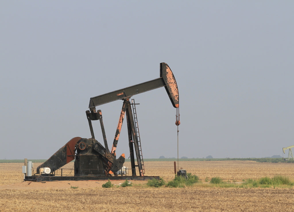 Oil Well Pump Jack in a farm field south of Ellsworth Kansas USA with blue sky on a Summer day