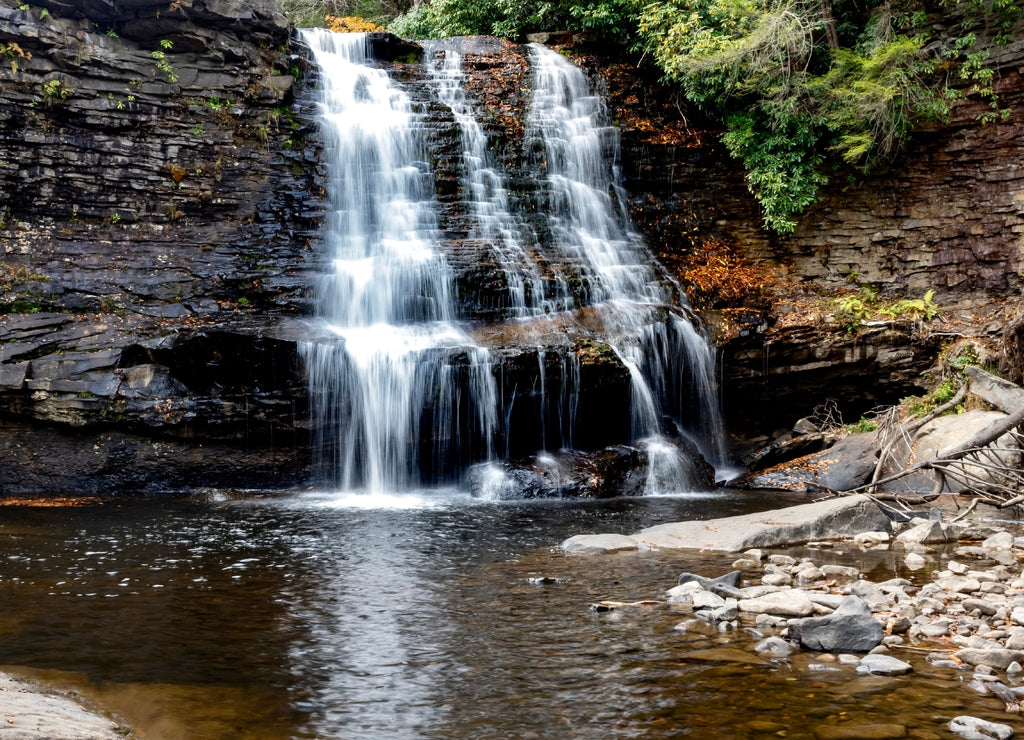 Muddy Falls in Swallow Falls State Park in Oakland, Maryland, the waterfall cascading and flowing down the side of the rocks in the autumn with leaves fallen in the water below