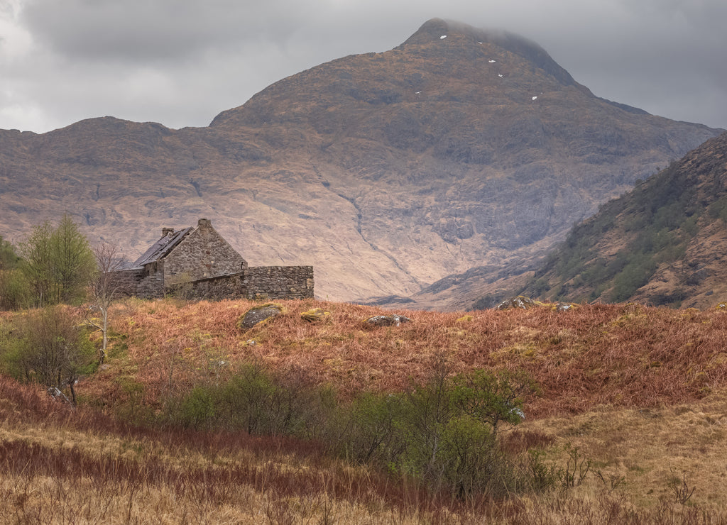 An isolated old stone bothy in a moody mountain landscape on the remote and rugged Knoydart peninsula in the Scottish Highlands, west coast Scotland