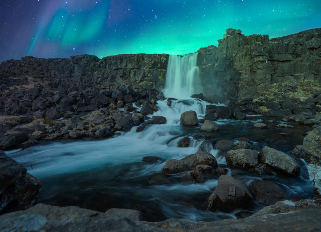 Northern lights/aurora borealis are dancing over the famous oxarafoss waterfall at night in thingvellir national park in Reykjavik