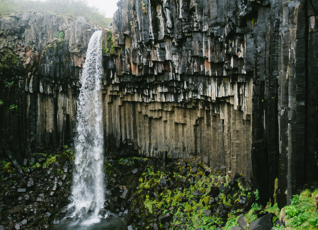 Mighty Svartifoss waterfall in Iceland under grey cloudy sky. Crystal clear white water and black basalt columns