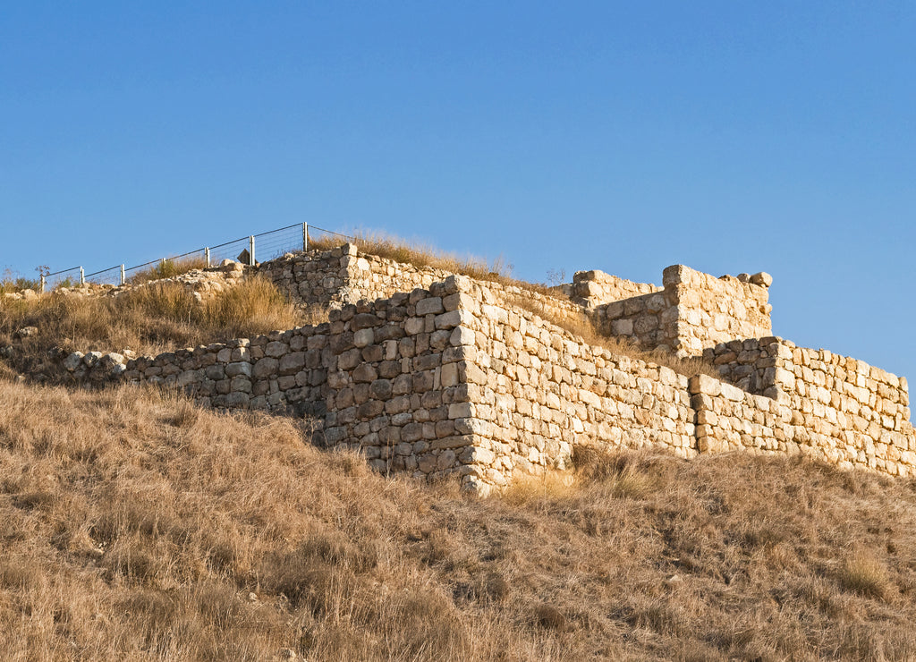 The stone city gates and retaining wall of biblical era Tel Lachish in Israel with the moon setting in a clear blue sky in the background