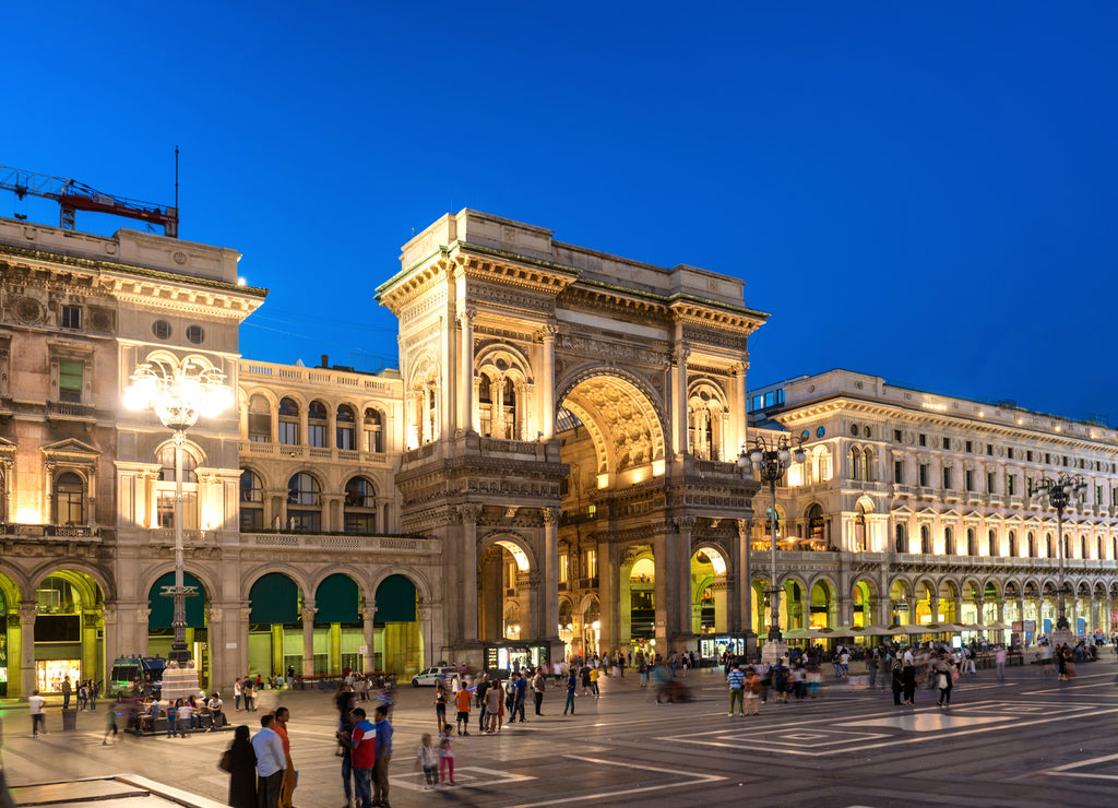 People walking near Vittorio Emanuele II gallery at Duomo square, Milan, Italy. Night view of street and buildings