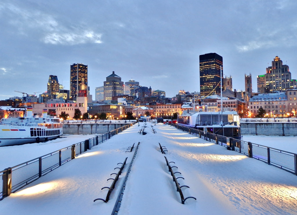 Snow-covered benches, pier, waterfront walkway, harbor, and downtown Montreal after sunset in winter - Montreal, Canada