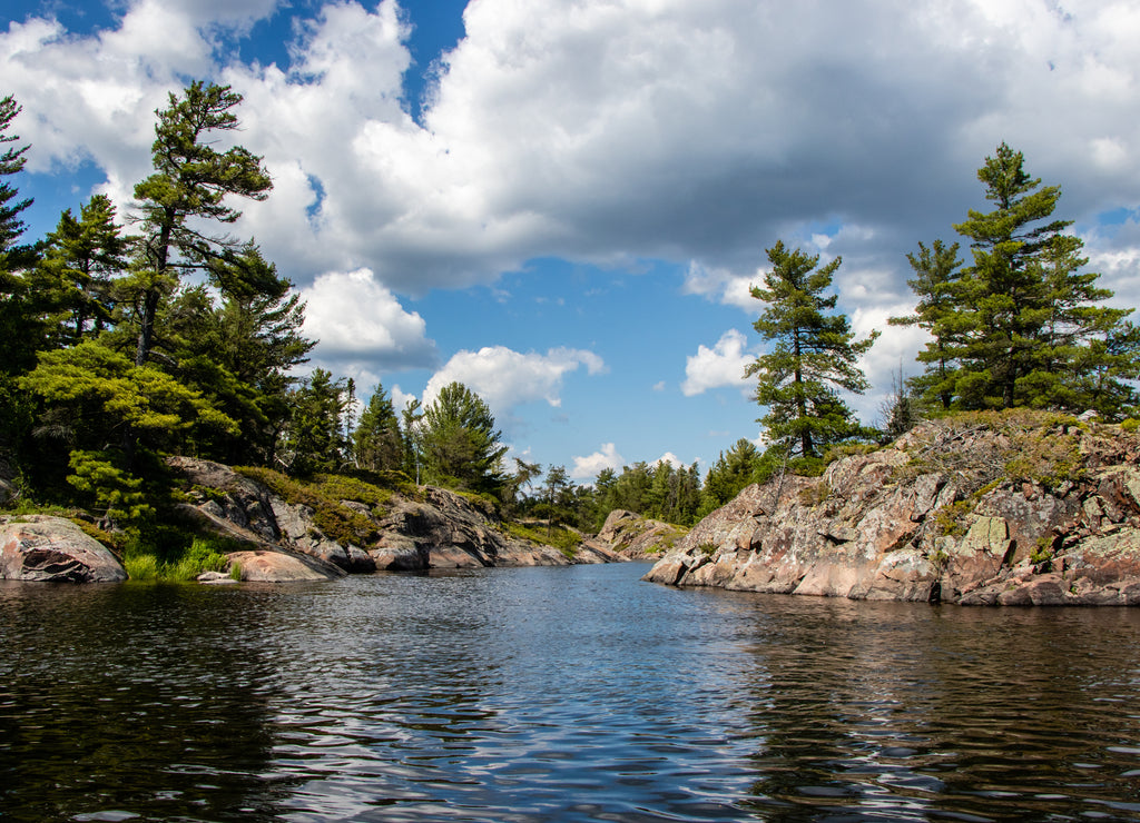 Rocks, trees, blue sky, white clouds and water on a summer day on the Bad River in Ontario, Canada