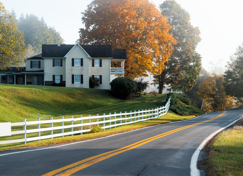 Roadside farmhouse house in countryside rural road highway in West Virginia, USA by mountain forest with colorful autumn fall trees foliage at sunrise morning