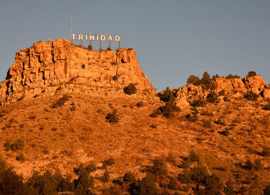 Low angle view of the city of Trinidad Colorado landmark sign with an early sunrise glow against the rocky butte and sky