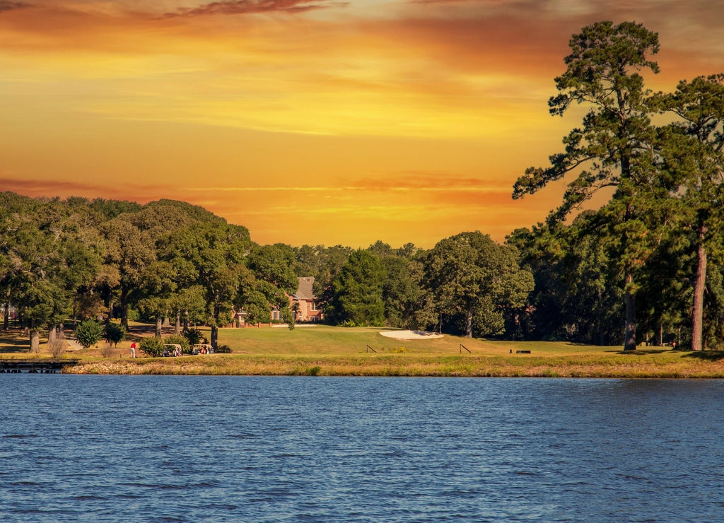 a gorgeous summer landscape on Houston Lake with blue rippling water surrounded by lush green trees, grass and plants with powerful clouds at sunset in Perry Georgia USA