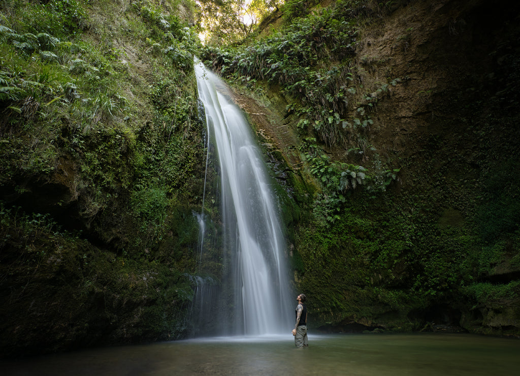 Caucasian man inside the water looking up Te Ana falls in Hawke's Bay, New Zealand