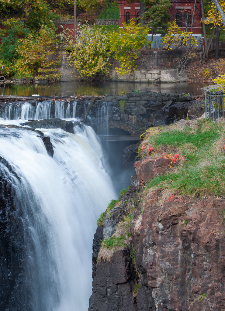 Waterfall in long exposure between rock with a red building in the background at Paterson Falls, New Jersey