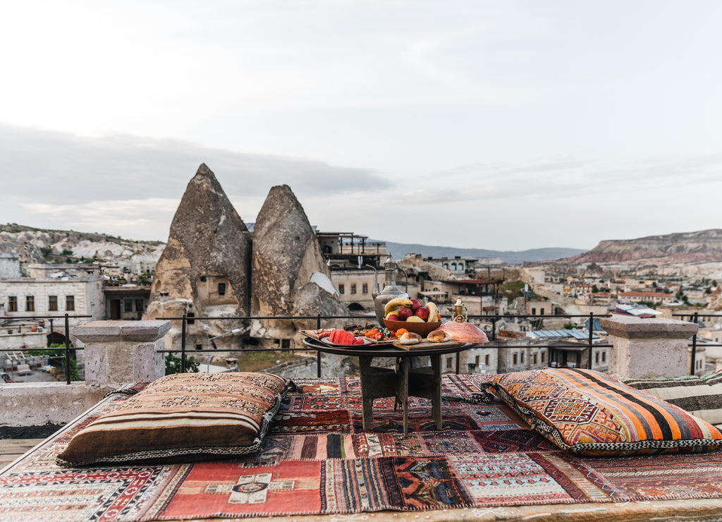 Round table, pillows and traditional carpet on terrace and beautiful scenic of buildings and rocks in Cappadocia, Turkey