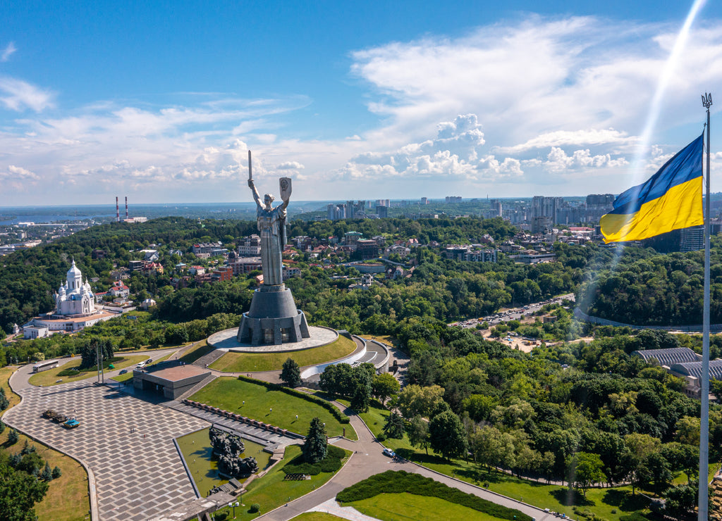 Aerial view of the Ukrainian flag waving in the wind against the city of Kyiv, Ukraine near the famous statue of Motherland