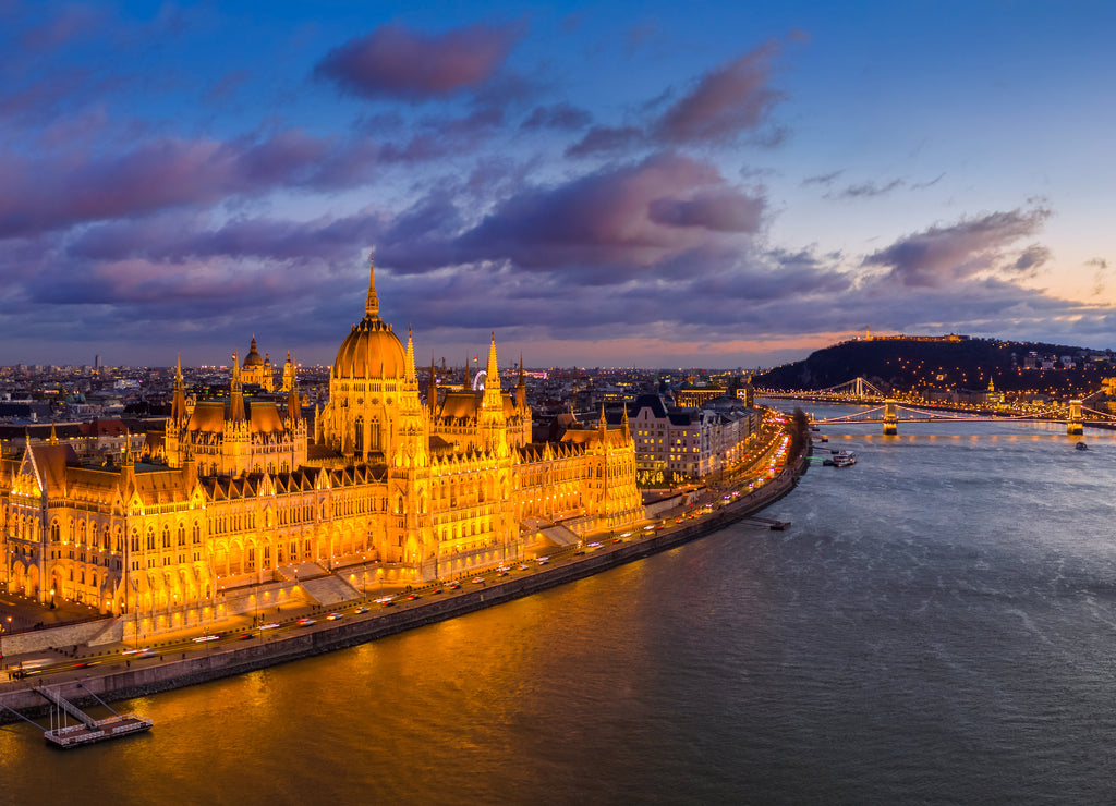 Budapest, Hungary - Aerial panoramic view of the beautiful illuminated Parliament of Hungary with Szechenyi Chain Bridge, Buda Castle Royal Palace and colurful clouds at background at sunset