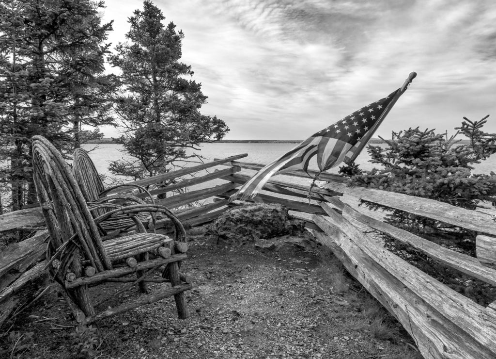Rustic willow twig chairs and American flag overlooking ocean. Acadia, Maine in black white