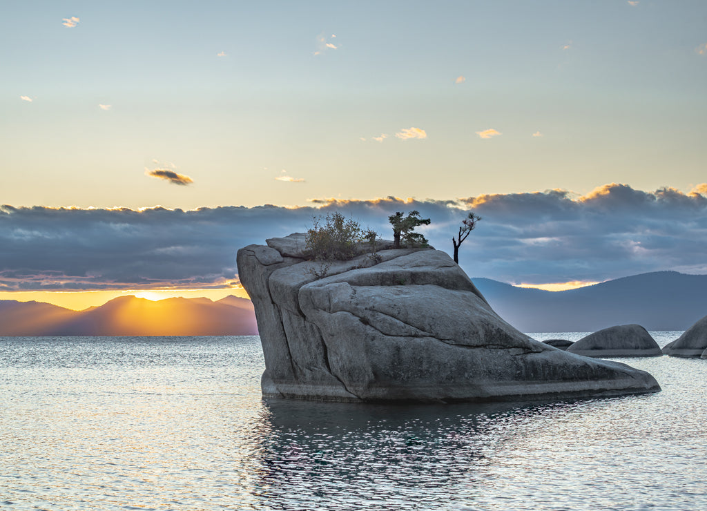 USA, Nevada, Washoe County, Lake Tahoe. Bonsai Rock in front of Sunset sun beans shining under a layer of clouds over the Sierra Nevada Mountains