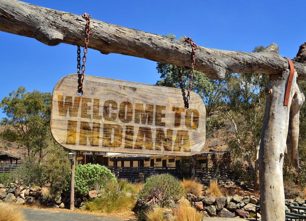 Old wood signboard with text " welcome to indiana" hanging on a branch