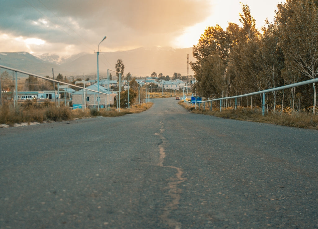 Cracked asphalt road surrounded by trees in a village in Armenia under the sunset sky