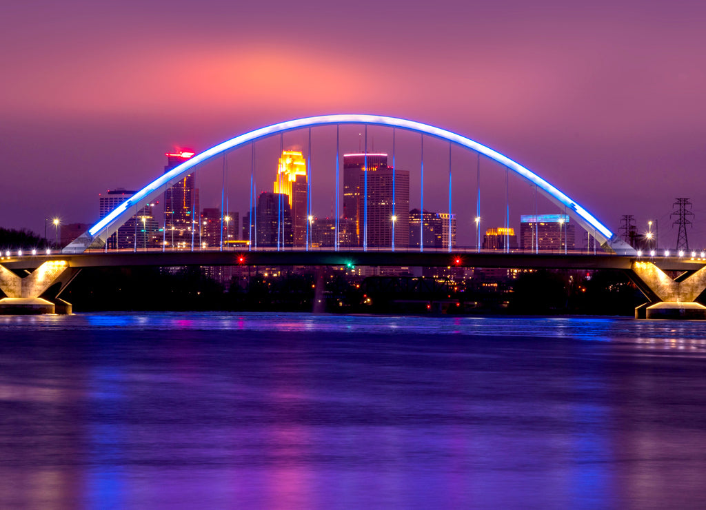Lowry Avenue Bridge colored blue at dusk with Minneapolis Skyline behind