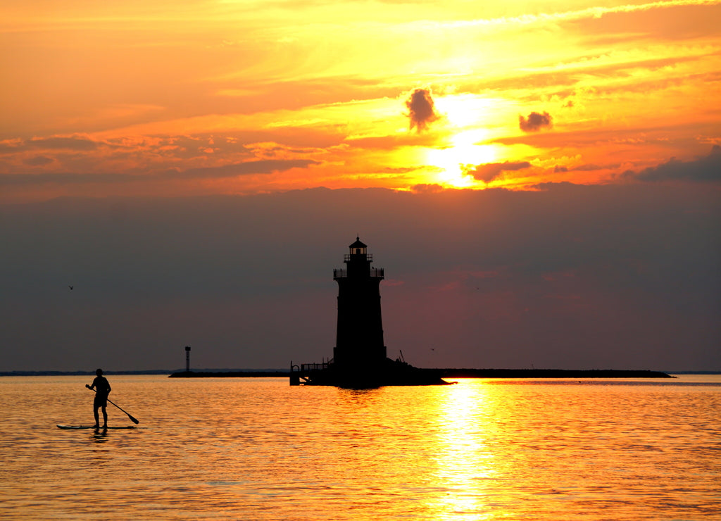 Silhouette of a light house and a man on a paddle board during sunset at Cape Henlopen State Park, Lewes, Delaware, U.S.A