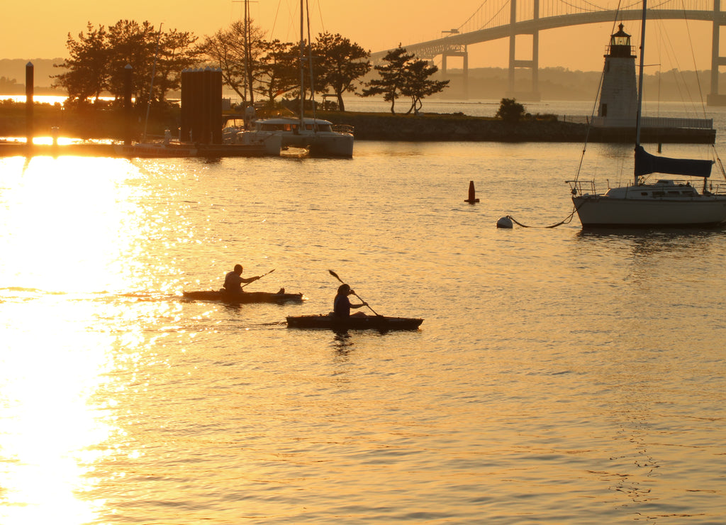 Two kayakers are out i the evening water, near the Newport Pell Bridge in Newport, Rhode Island