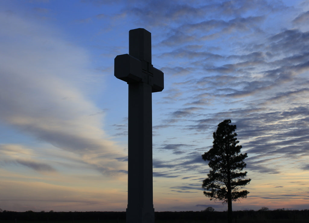 Father Padilla's Cross with a tree and clouds that are Silhouettes with a colorful Sunset west of Lyons Kansas USA out in the country