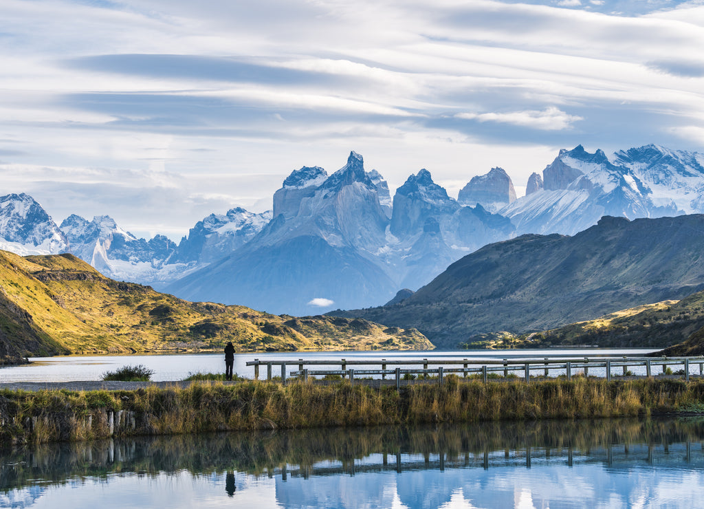 Beautiful panoramic view small people standing at the dock from the lake with Cuernos, horn mountains peak with lenticular cloud in autumn, Torres del Paine national park, south Patagonia, Chile