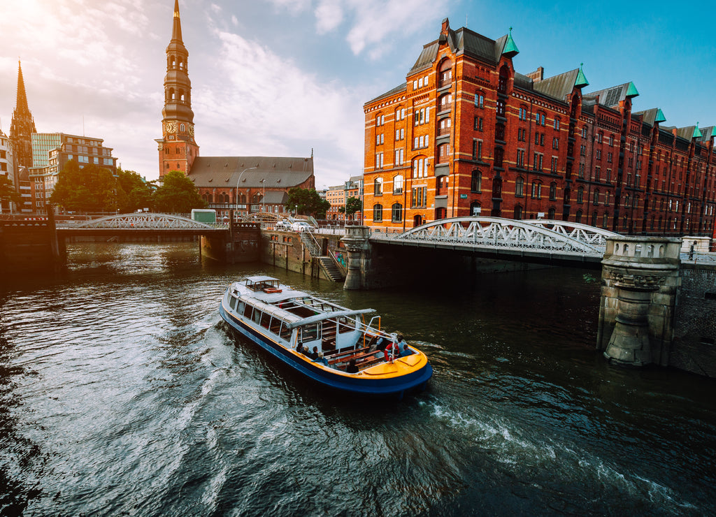 Touristic cruise boat on a channel with bridges in the old warehouse district Speicherstadt in Hamburg in golden hour sunset light, Germany