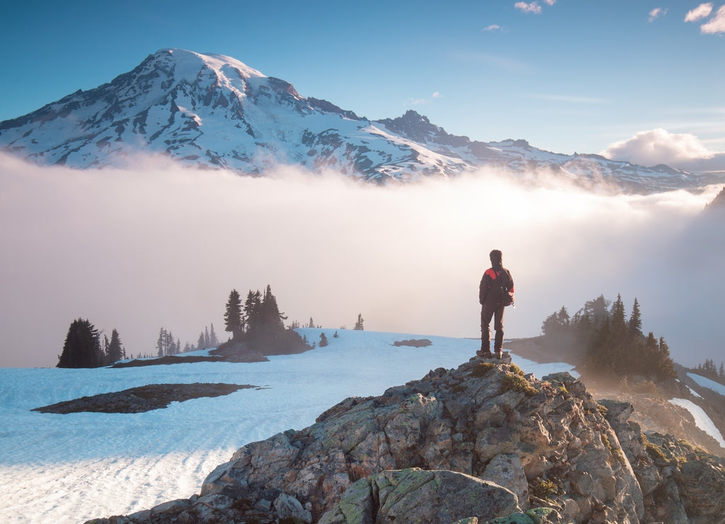 Man on the mountain peak looking on mountain valley with low clouds at colorful sunrise in autumn in Mount Rainier National park, Washington, USA. Landscape with traveler, foggy hills. Alone tourist