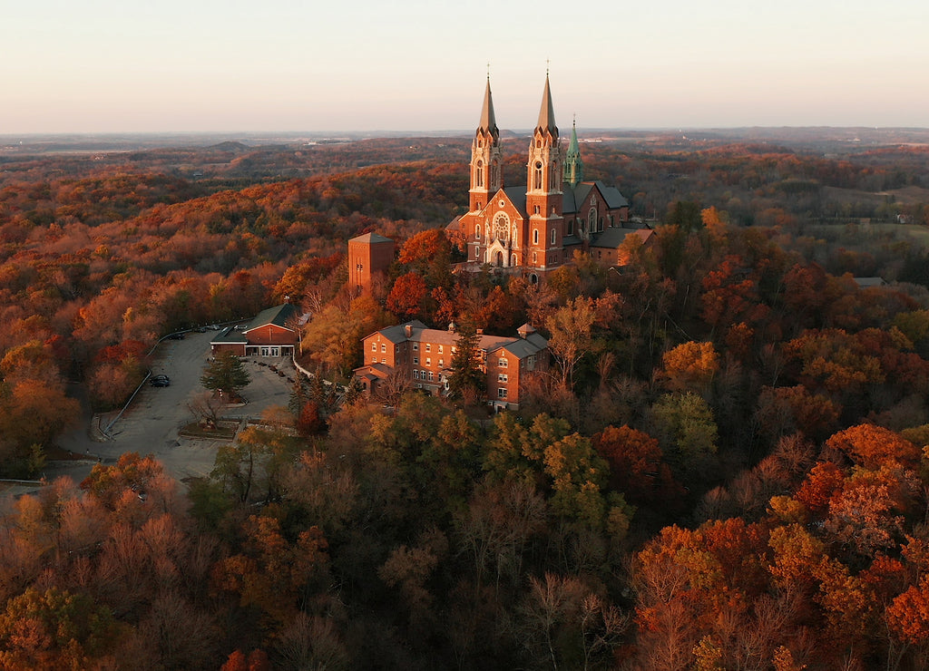 Aerial view of a church on the top of hill and autumn forest, red foliage . Fall season, autumn colors. Countryside, Wisconsin. Drone shots at sunset