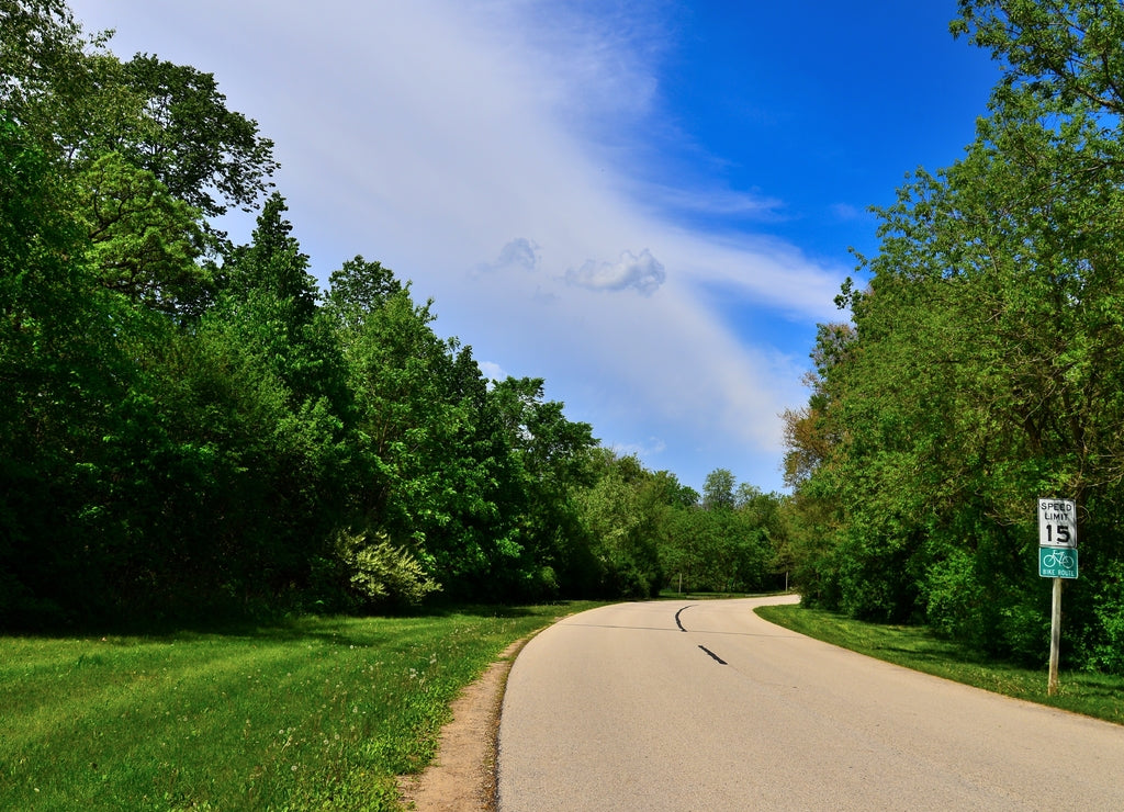 The slow tree lined roadway through Case Eagle Park in Rochester Wisconsin on a sunny summer afternoon with beautiful light clouded skies