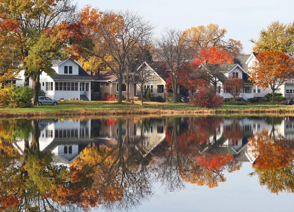 Autumn in a city background. Fall cityscape with private houses neighborhood along a pond. Colorful trees and houses reflected in a water. Midwest USA, Wisconsin. Classic american middle class homes