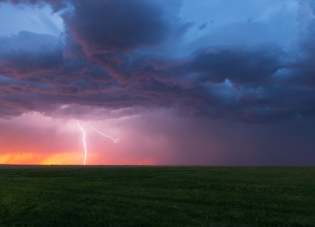 Lightning bolt strikes at dusk on the Wyoming / Colorado border with dark storm clouds overhead. The orange glow of sunset is seen on the horizon