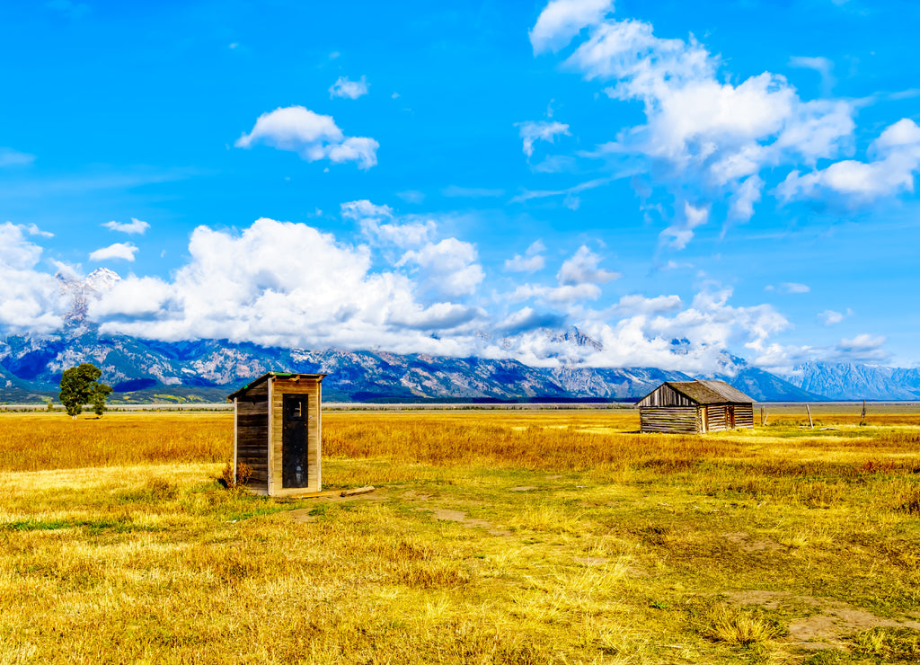 An Outhouse at Mormon Row with in the background cloud covered Peaks of the Grand Tetons In Grand Tetons National Park near Jackson Hole, Wyoming, United States