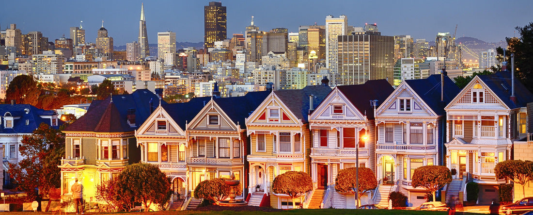 The Painted Ladies of San Francisco, California sit glowing amid the backdrop of a sunset and skyscrapers 2000pc Panoramic Puzzle