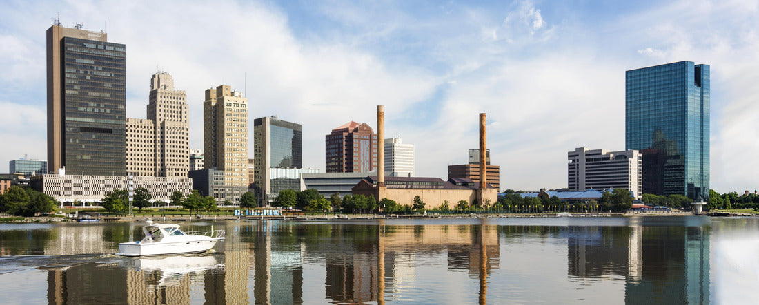 A downtown Toledo Ohio's skyline reflecting into the Maumee river with a power boat cruising by. A beautiful blue sky with white clouds for a backdrop 2000pc Panoramic Puzzle