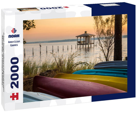 Noah Jigsaw Puzzle A lone brown pelicanon a post at sunset with colorful canoes on the shore of Mobile Bay, at Fairhope Alabama 2000 pieces