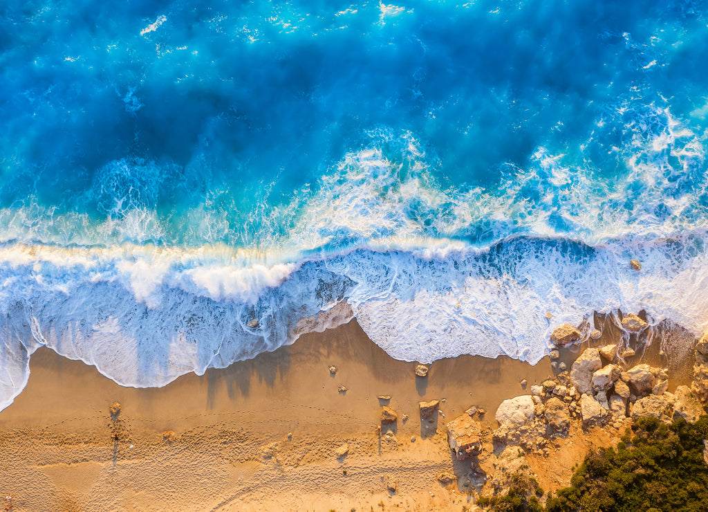 Top view of the golden beach and fluorescent blue sea of Milos Beach on the island of Lefkada, Greece, with high waves and long shadows during summer sunset time