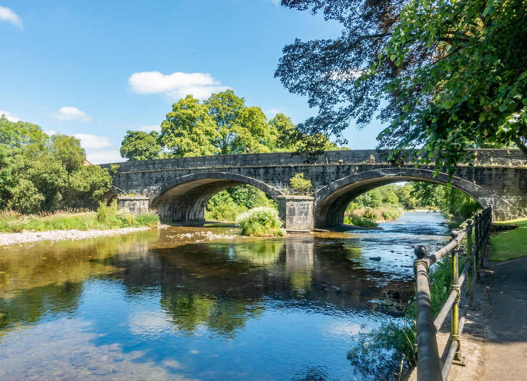 The upper reaches of the River Severn in the public park of Llanidloes, mid Wales, UK with the stone built bridge in the distance