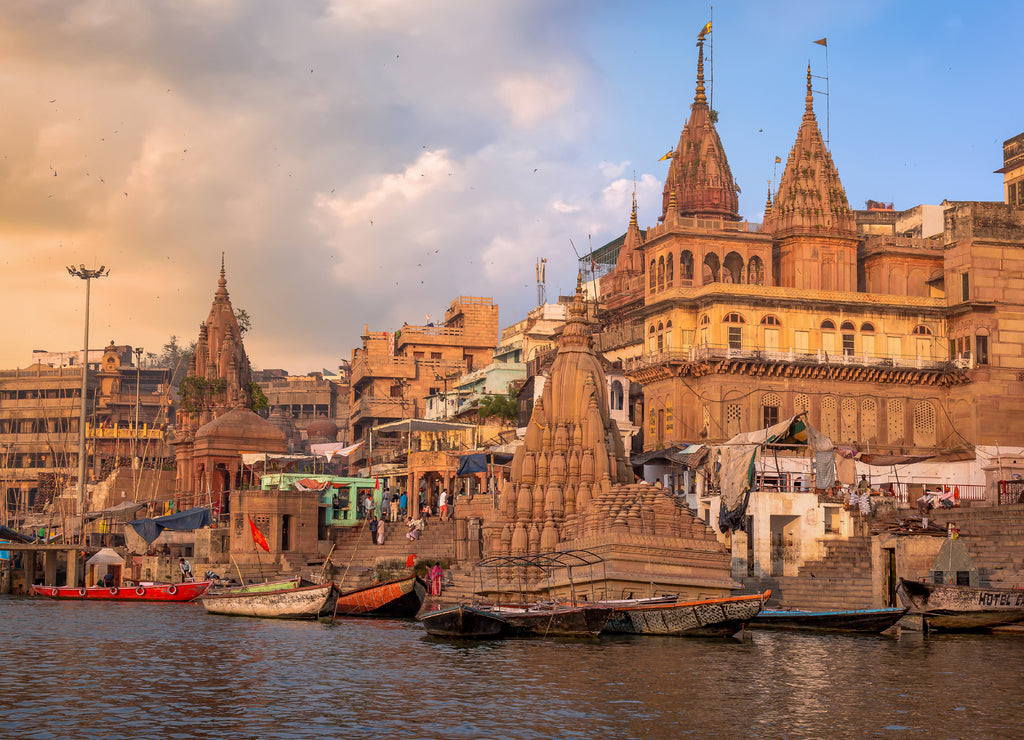 Varanasi city with old architectural buildings and temples along the Ganges river ghat as viewed from a boat at sunset