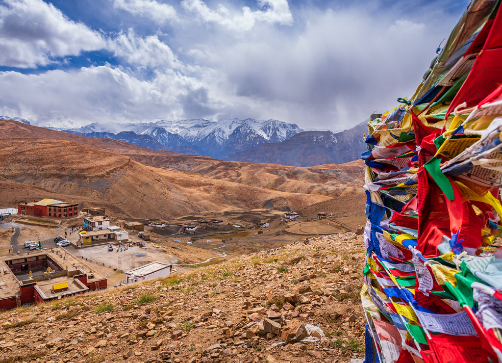 Colorful prayer flags flying in winds with Komic village nestled in Himalayas mountains in background in Spiti valley of Himachal Pradesh, India
