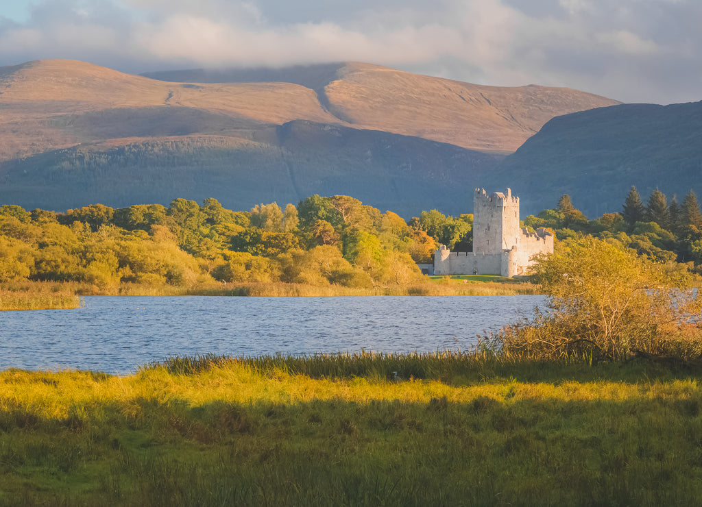 Golden hour sunset light on scenic mountain landscape of the historic medieval Ross Castle on Lough Leane lake in Killarney National Park, County Kerry, Ireland
