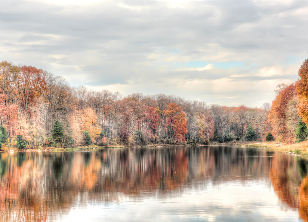 Sunset at Lake Woodglen in Fairfax, Virginia near residential neighborhood, with orange foliage autumn trees forest, water reflection, houses, rocky beach shore