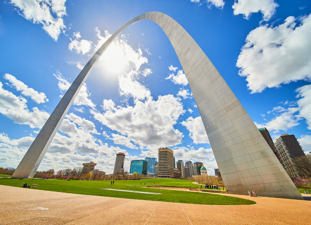 Skyline viewed under St. Louis Gateway Arch with vibrant sky and sun