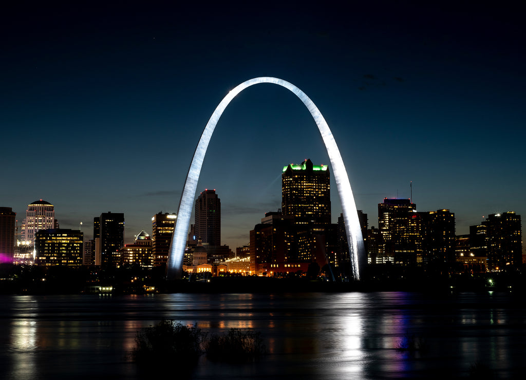 St Louis Gateway Arch brightly lit and shining at night, city skyline in background, reflecting in Mississippi River
