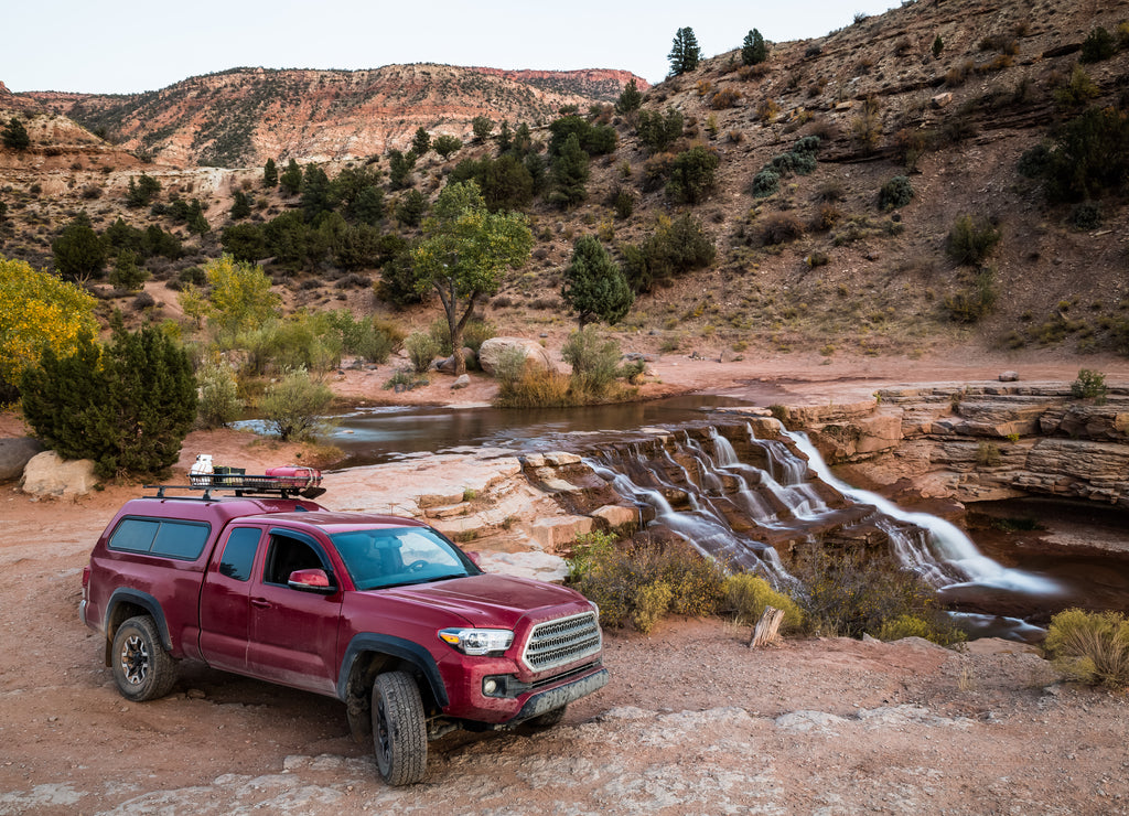 Red pickup camping rig on rocky trail near waterfall in southern Utah