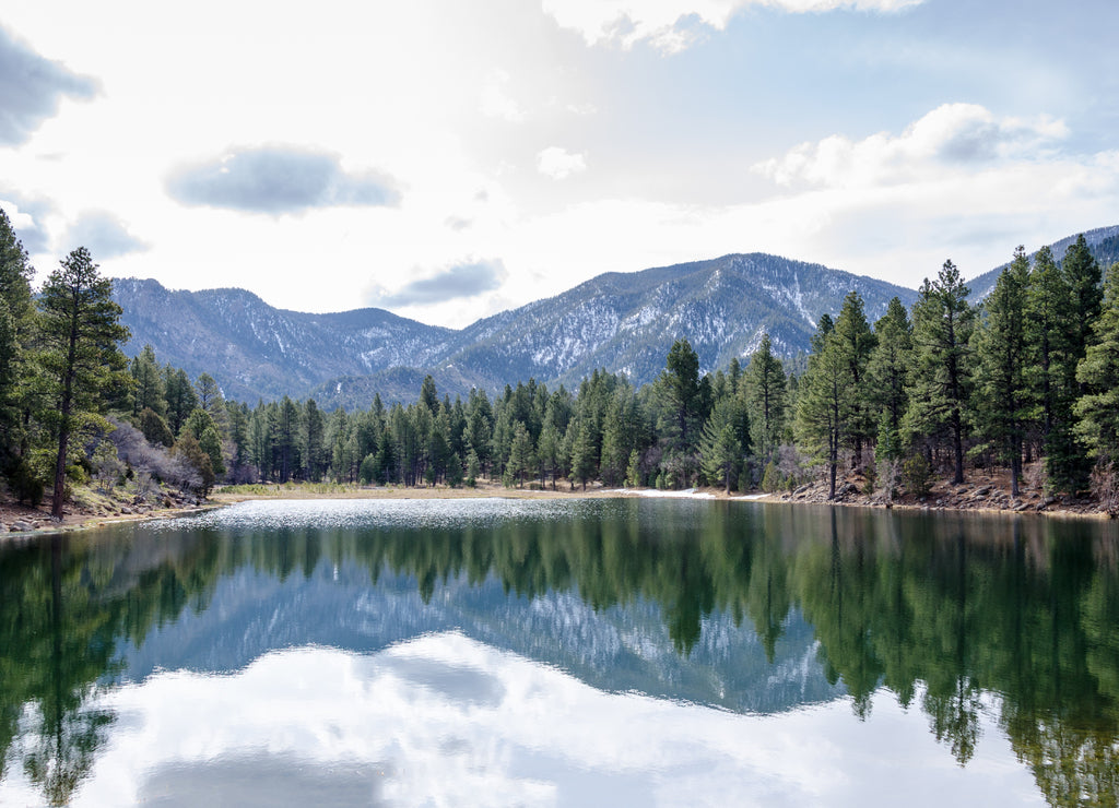 Trees and snow capped mountains reflected in lake in Dixie National Forest, Utah