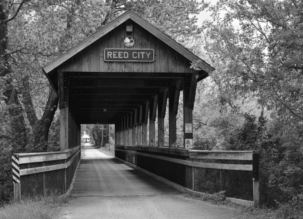 Covered wooden foot bridge over small peaceful creek in Reed City, Michigan in black white